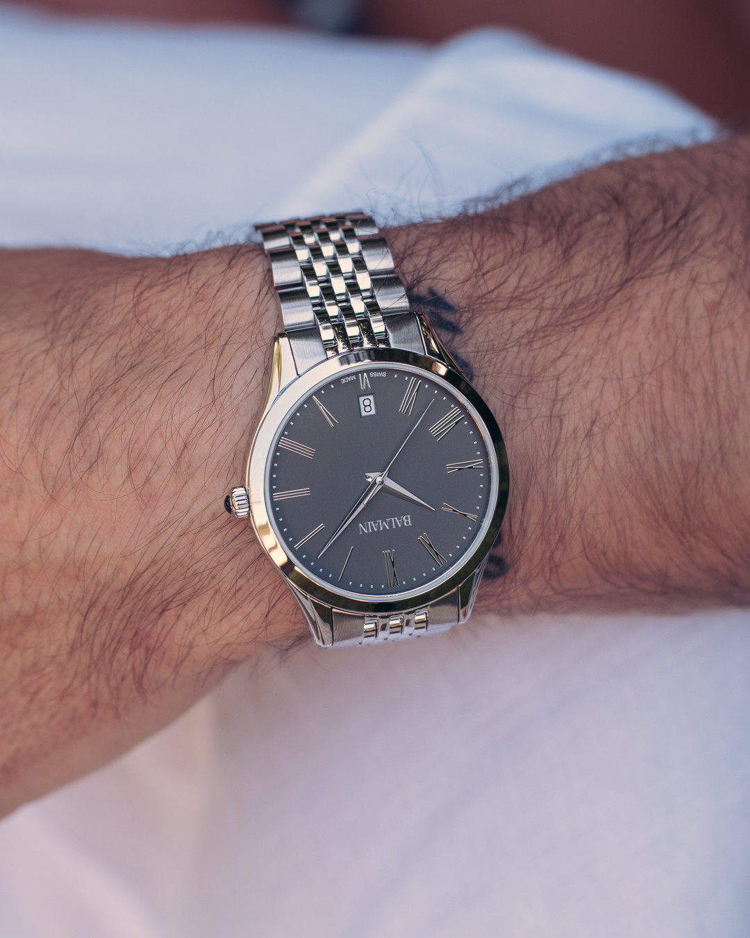 Close-up of a man’s wrist wearing the Balmain Classic R B4101.31.61 watch. It has a 41mm round stainless steel case, a sleek grey dial, and a matching metal bracelet. This was captured in natural light.