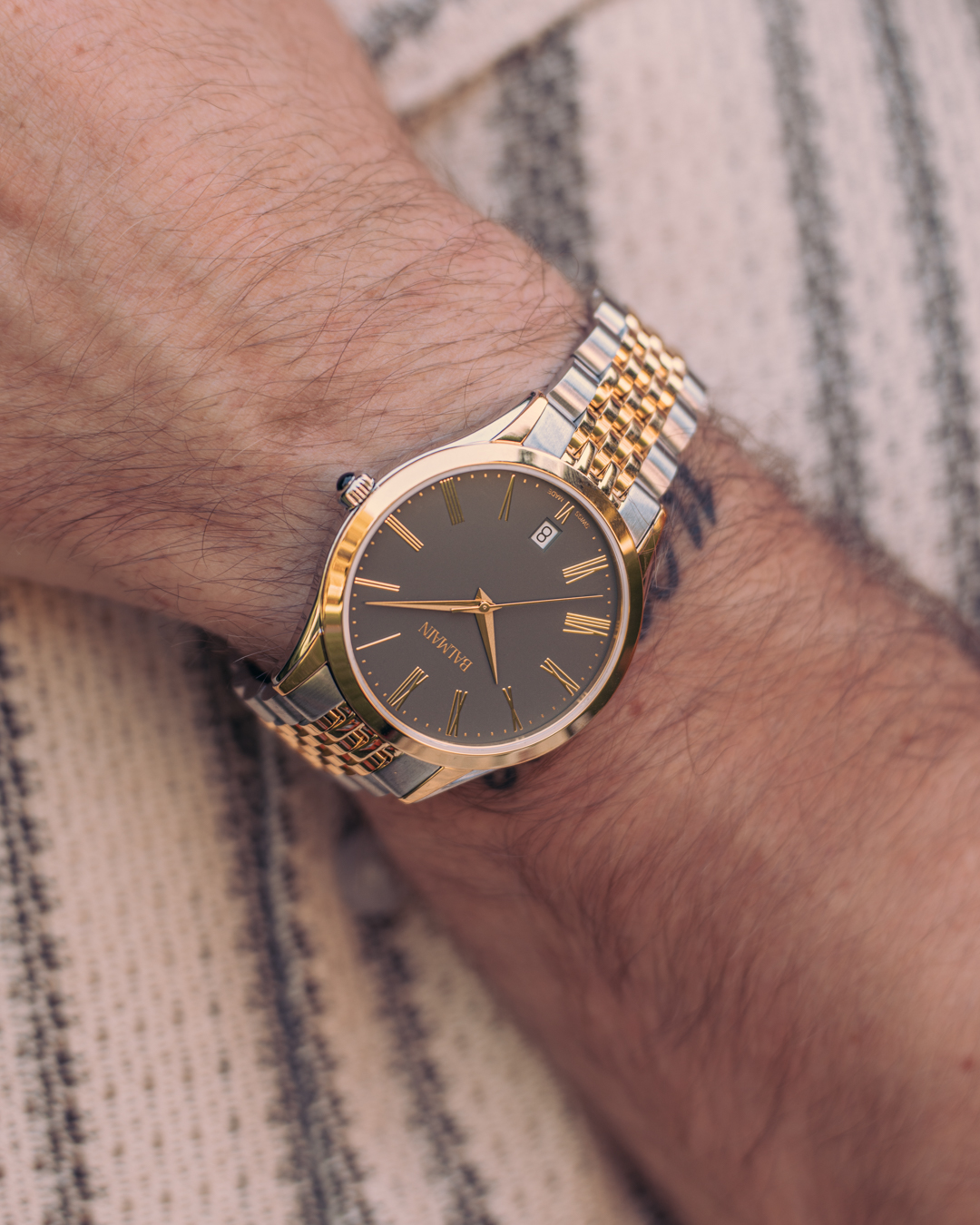 Close-up of a man’s wrist wearing the Balmain Classic R B4102.31.61 watch. It has a 41mm round bicolour case made of stainless steel and yellow gold PVD, a sleek grey dial, and a matching metal bracelet.