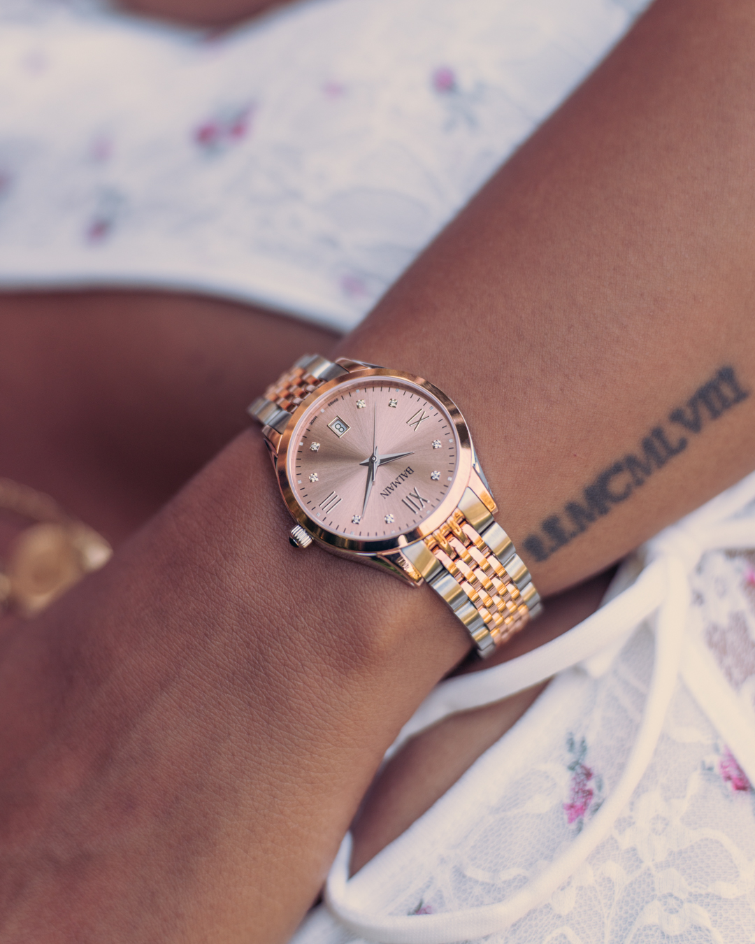 Close-up of a woman’s wrist wearing the Balmain Classic R B4318.31.45 watch. It features a 34mm round two-tone case made of stainless steel and rose gold PVD, a rose dial set with 8 Top Wesselton diamonds, and a matching metal bracelet.